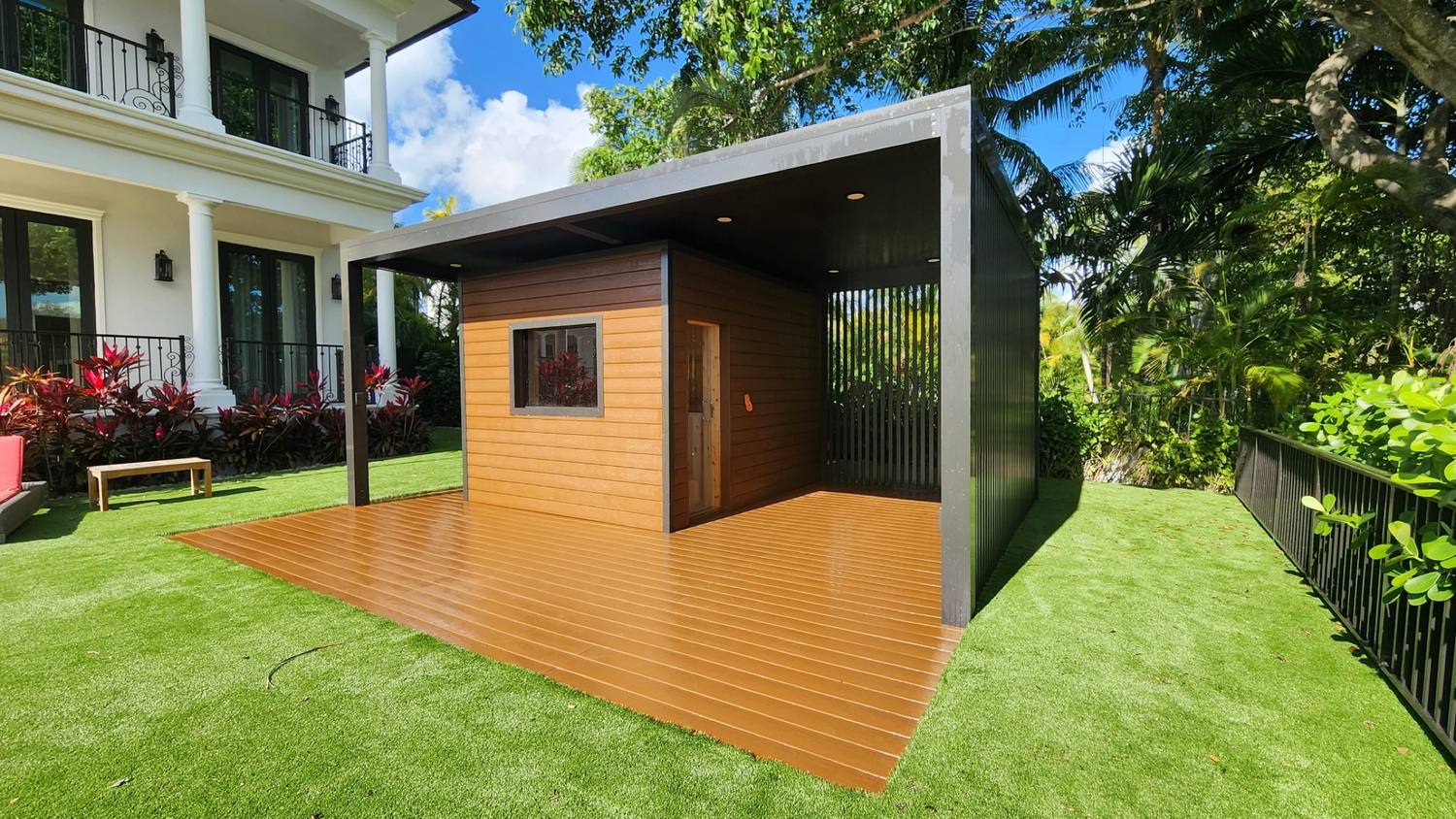 Black-clad garden studio on a timber deck, lawn and house behind, Coral Gables