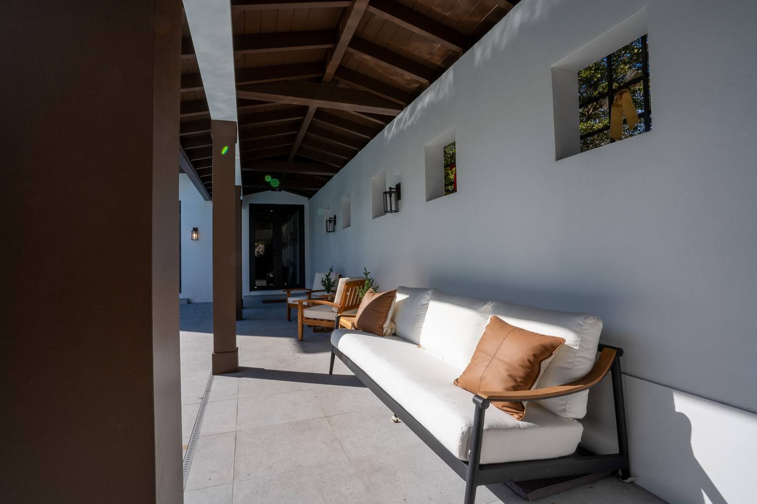 A covered loggia with a wood-beamed ceiling, wall lanterns and an outdoor sofa