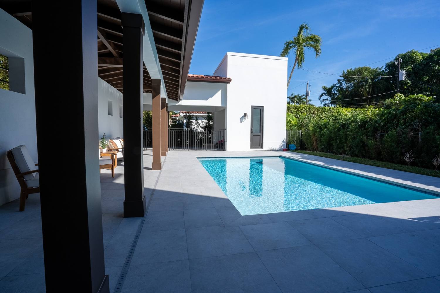 The pool deck seen from under the covered loggia, a hedge along the lot line