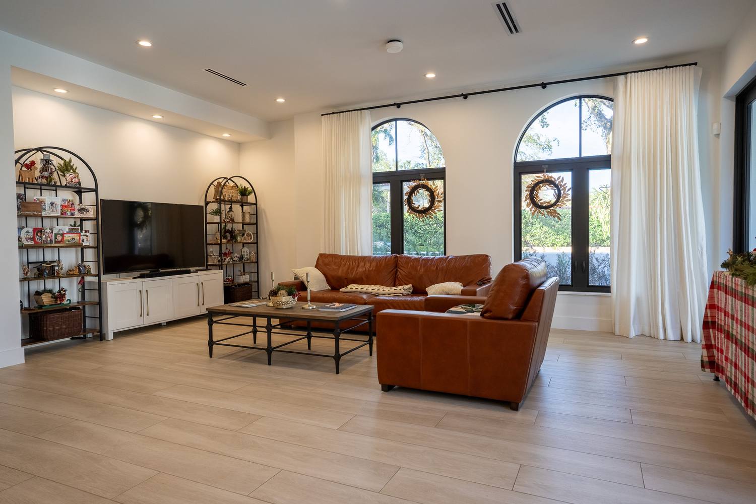A living room with a leather sofa and armchair under two tall arched windows