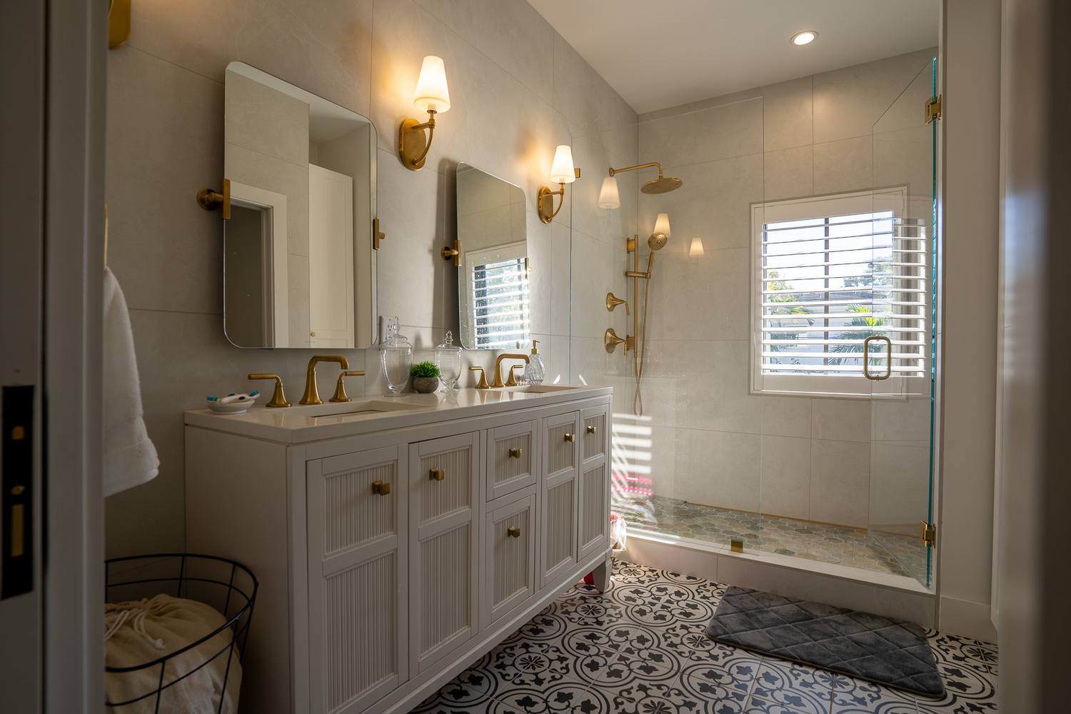 A double vanity with brass faucets and sconces beside a glass walk-in shower