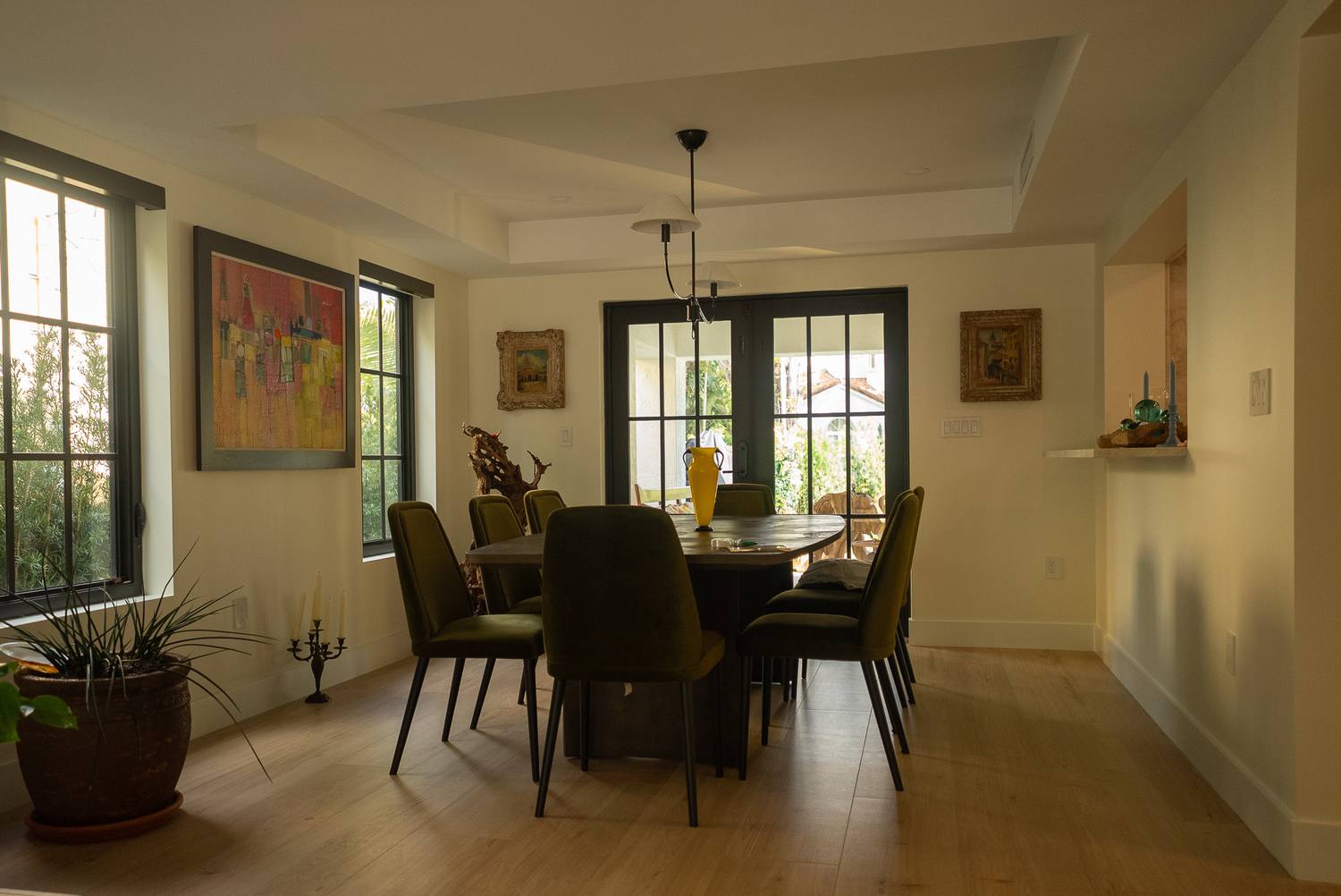 A dining room under a tray ceiling with a pendant light, olive-green chairs and French doors