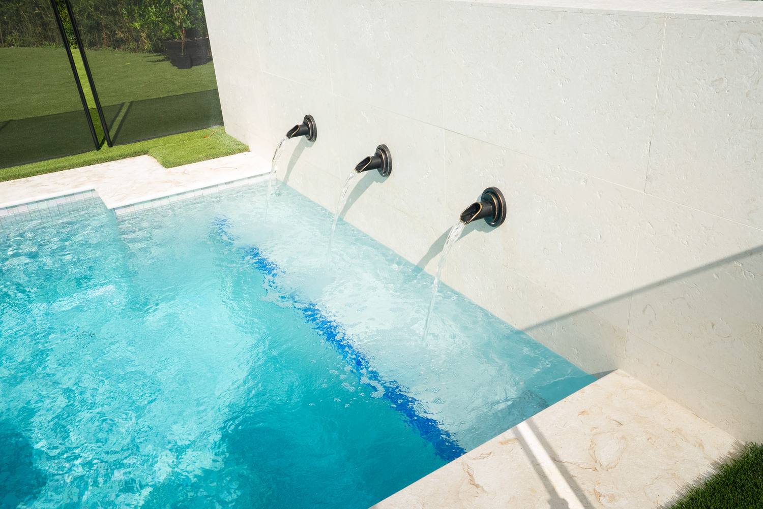 Three metal spouts pouring into a turquoise pool set against a pale stone wall
