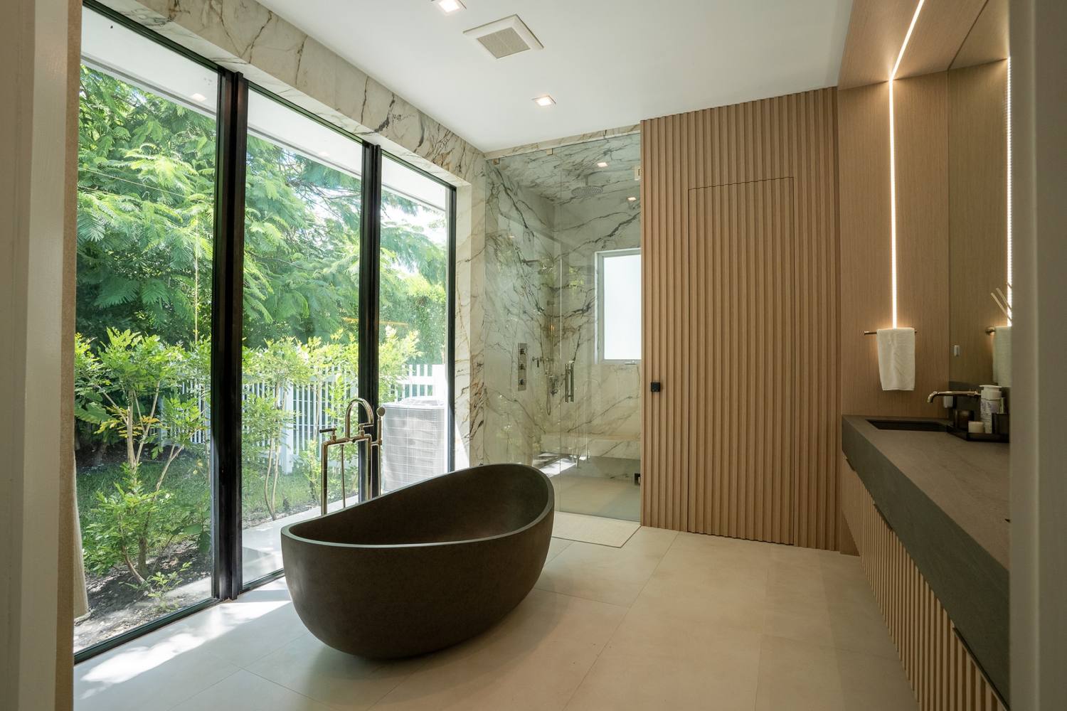 Primary bath with a stone tub, a vanity and a marble shower behind glass