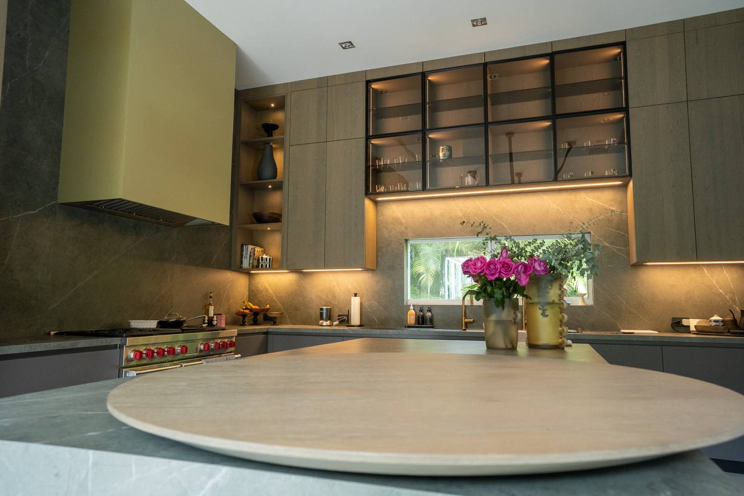Kitchen island with a round pale stone top in front of the range wall