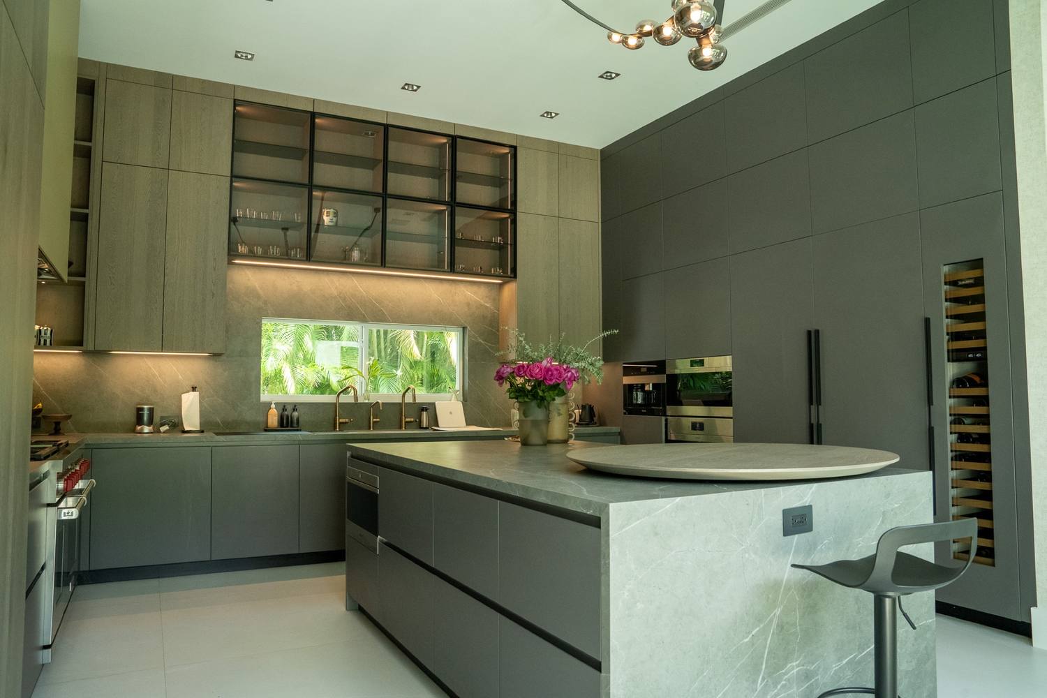 Kitchen with dark cabinetry, glass-front upper cabinets and a stone island with a round top