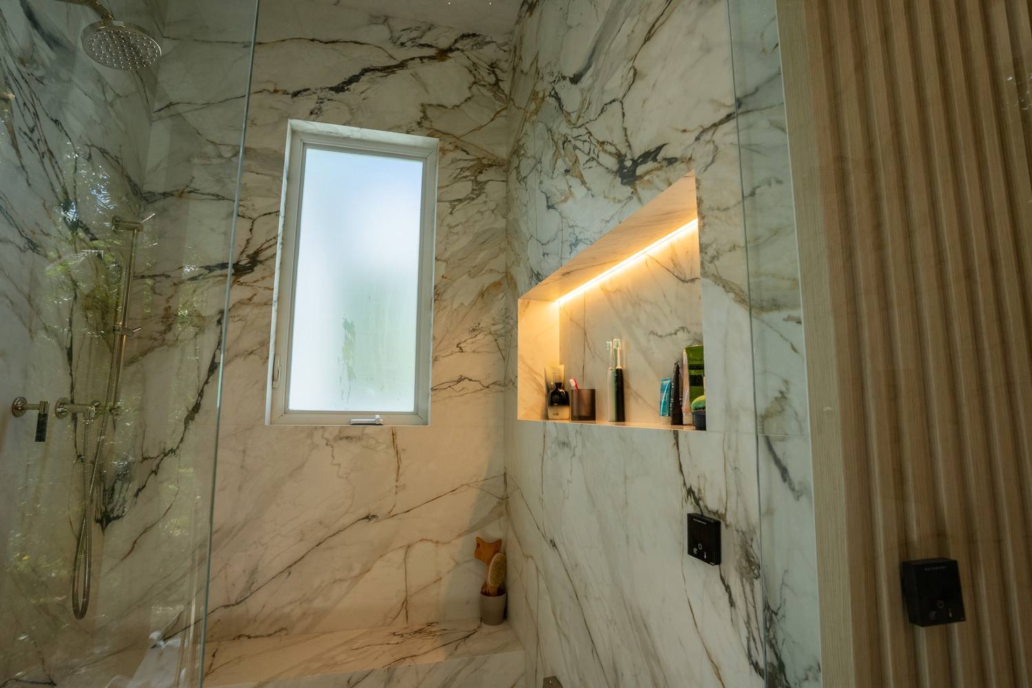 Shower walls in veined marble with a lit niche and a frosted window