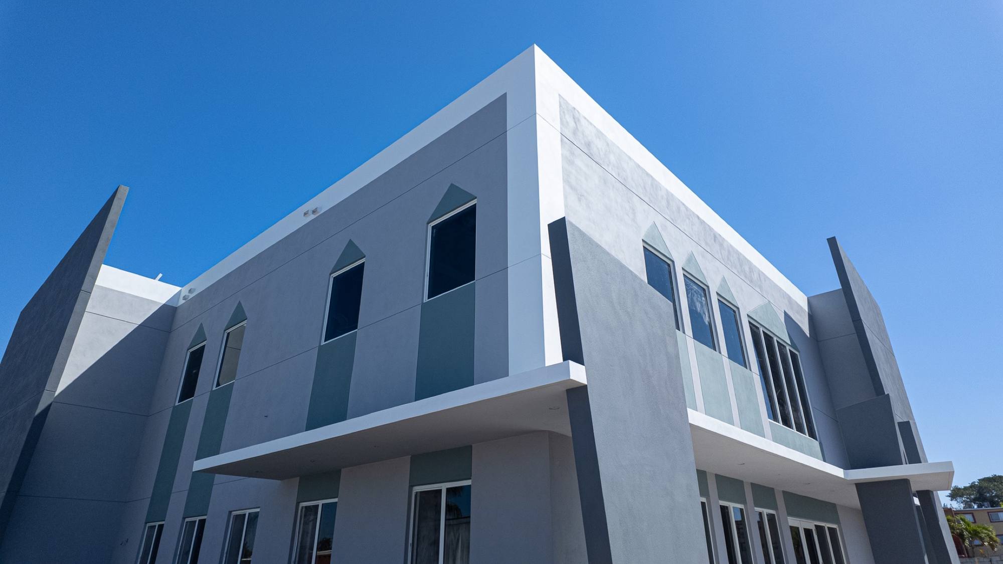 Two-story office building in grey stucco with a white band, from the street, Opa-locka