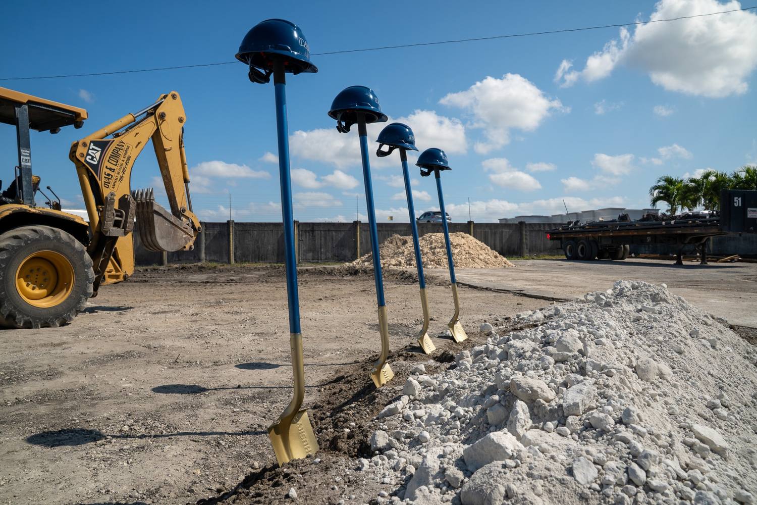 Groundbreaking shovels with DAG hardhats, second angle with the excavator and the site fence