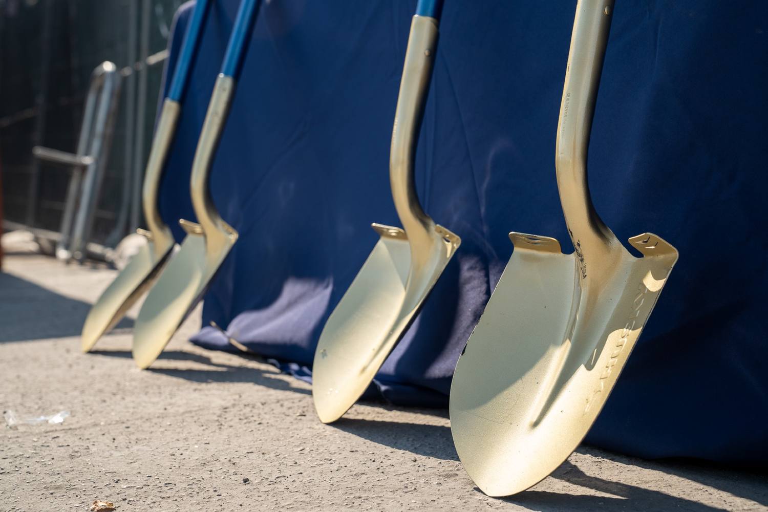 Gold groundbreaking shovels lined up against the table under the banner