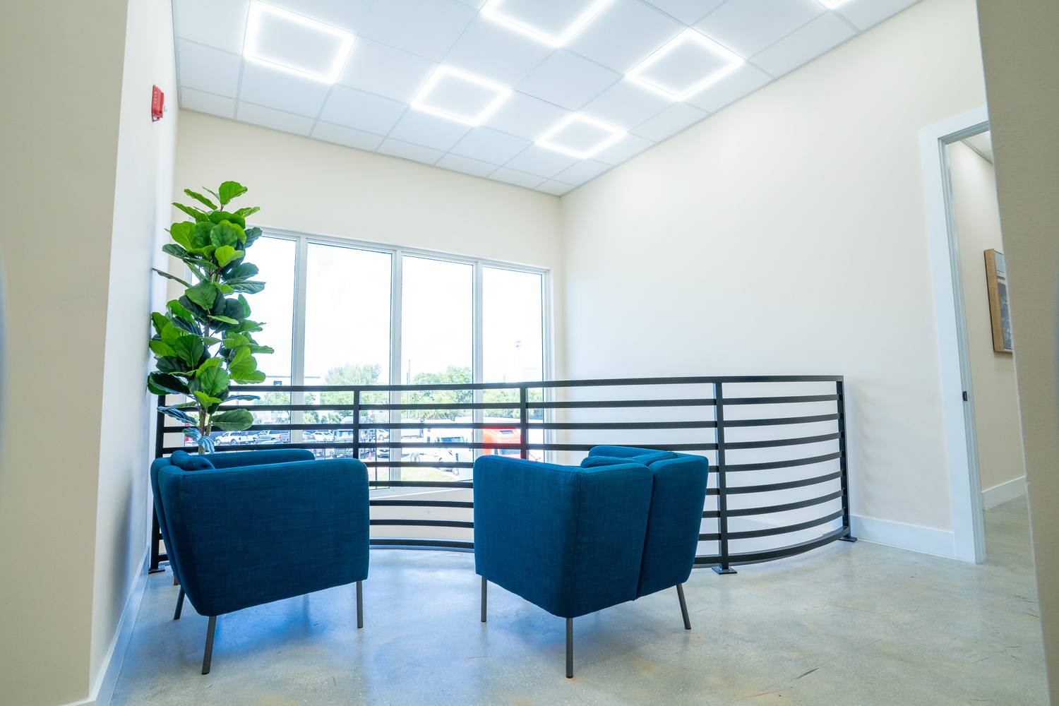 Two blue armchairs at a curved metal rail beside tall windows, upstairs