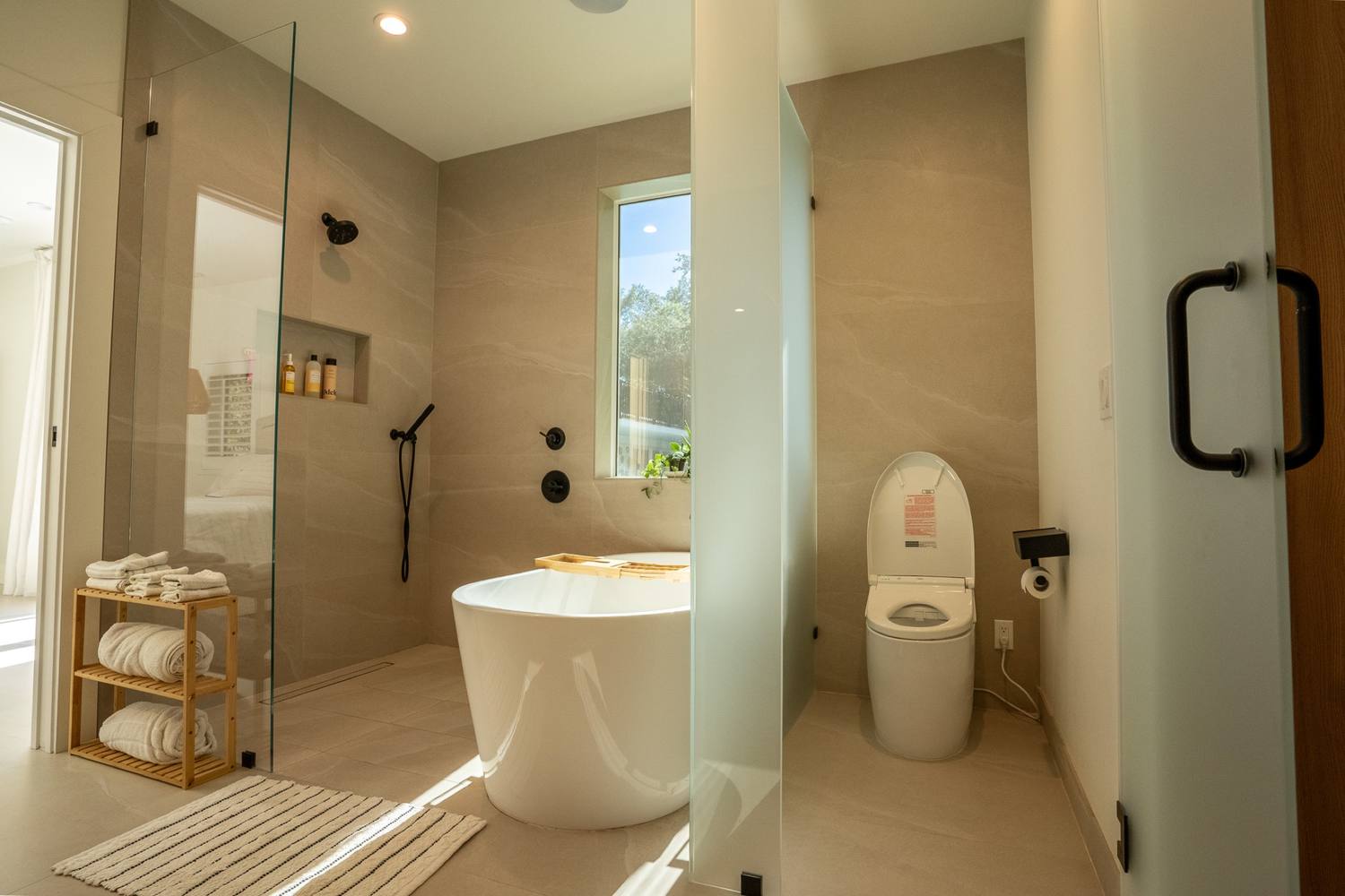 Primary bathroom with an open glass shower beside a freestanding tub under a window